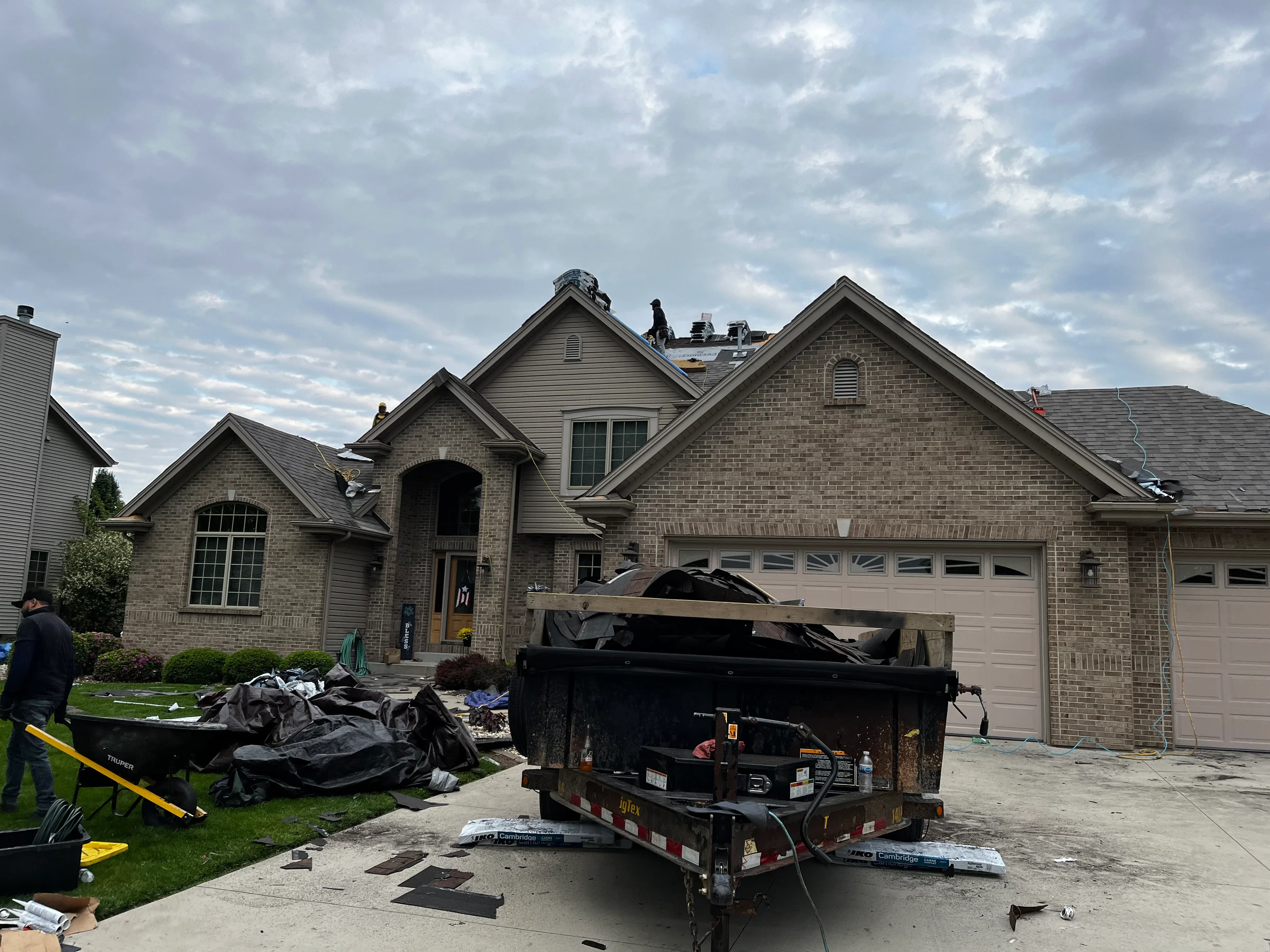 Brick home with multiple roof peaks during active roof replacement with equipment and debris removal