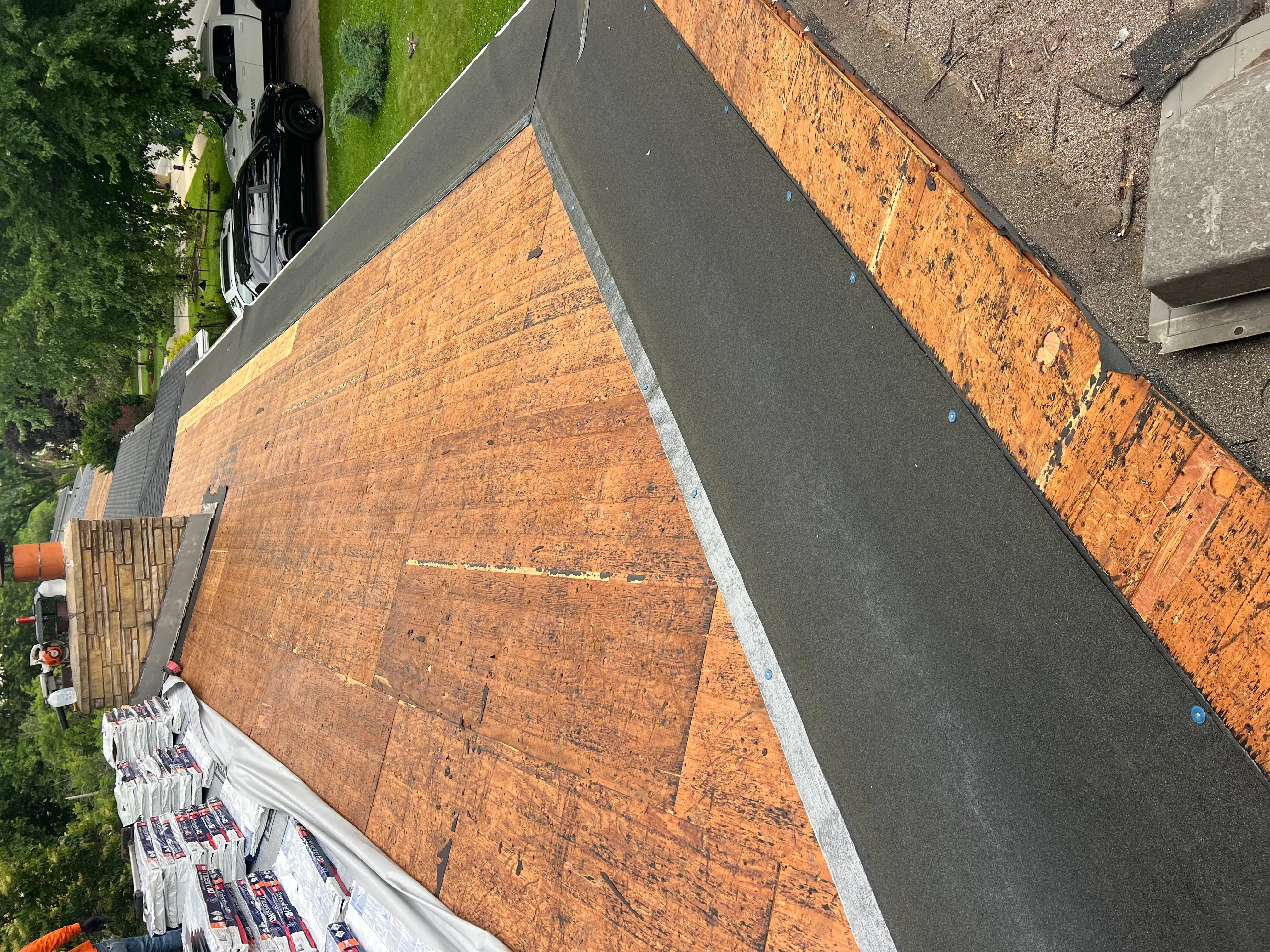 New asphalt shingle roof installation with metal flashing and brick chimney detail