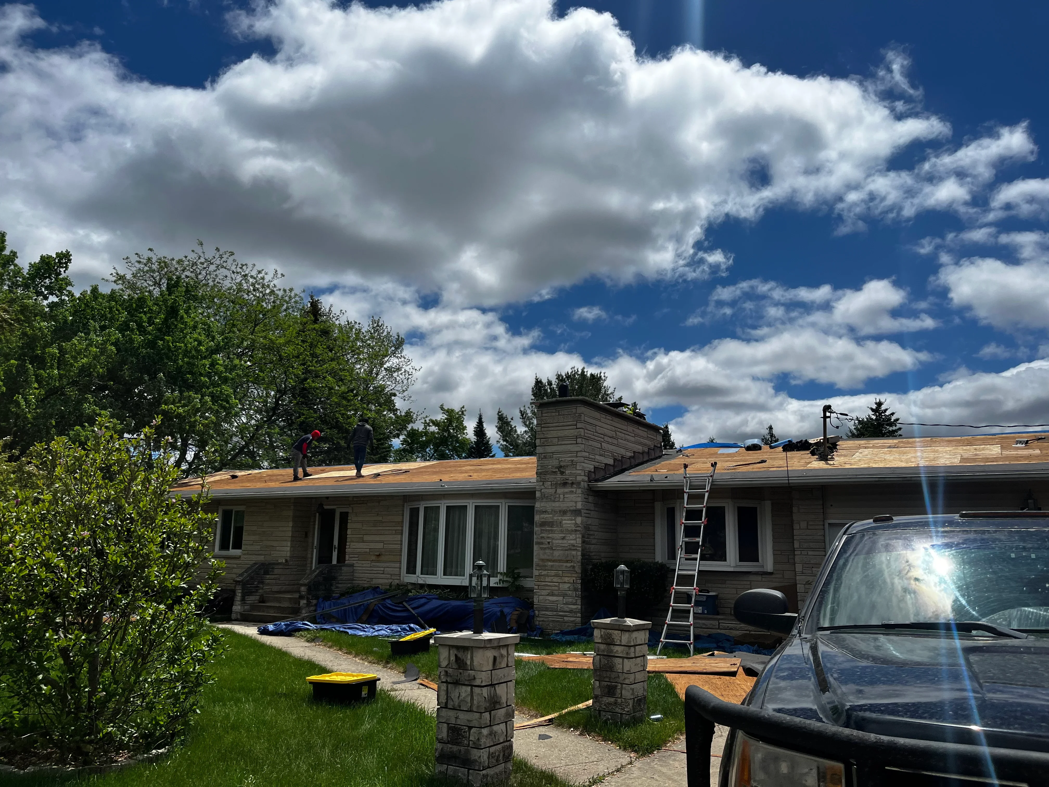 Residential roof replacement in progress with new wood sheathing and work crew on site