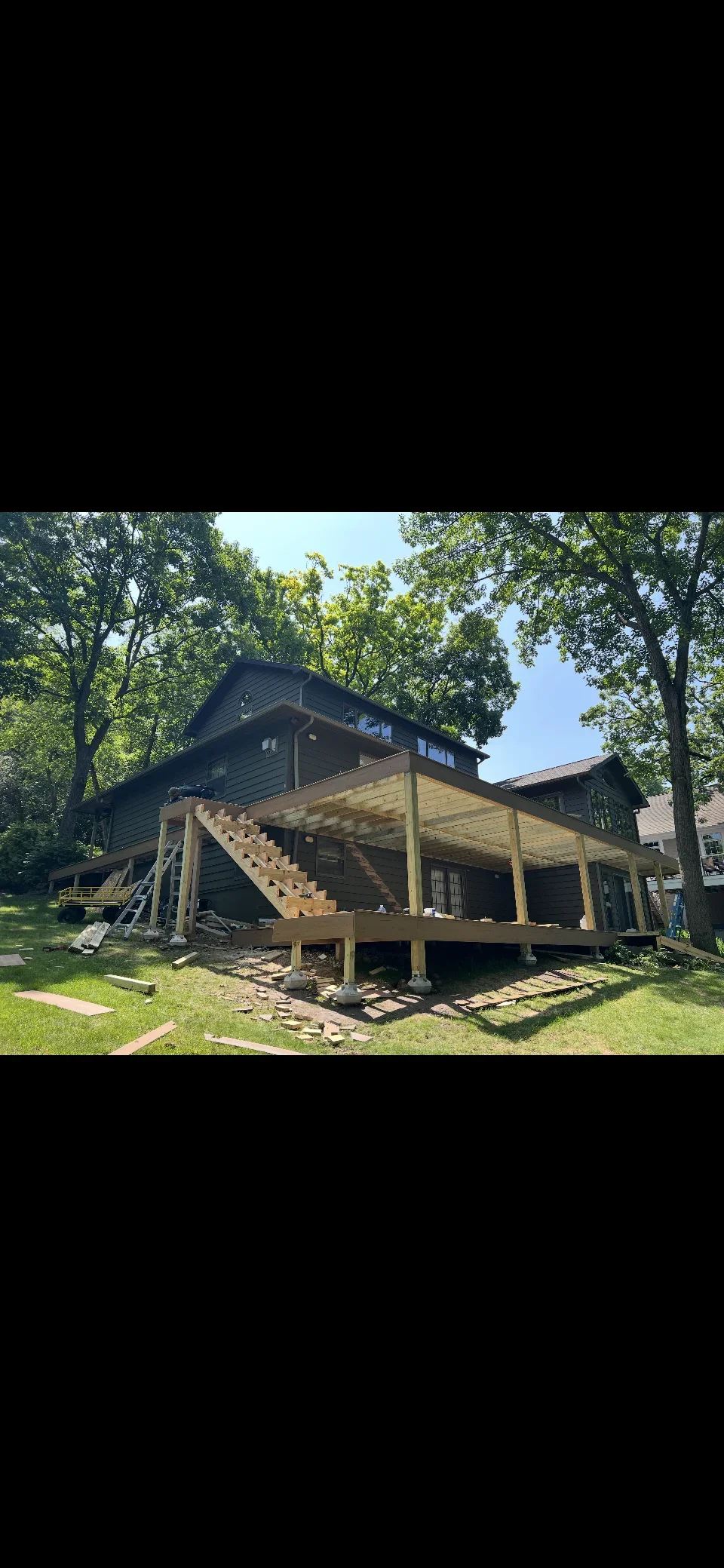 Dark-sided home with new wooden deck and stairs under construction in wooded setting